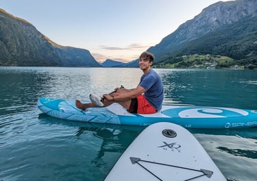 Man paddleboarding on a stand-up board in a calm Norwegian fjord surrounded by mountains