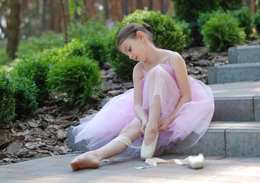 A young girl in a ballerina tutu fixes her ballet slipper.