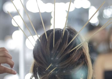 Peluquero profesional peinando un elegante recogido castaño con palitos de bambú frente a un espejo 