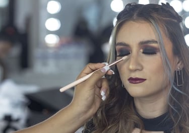 Maquilladora profesional aplica sombra de ojos ahumada oscura a una mujer en un estudio de belleza.