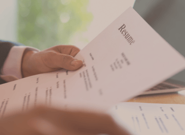 a person holding a resume in front of a laptop
