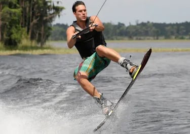 A man performing a jump on a wakeboard across a lake during a water sports session.