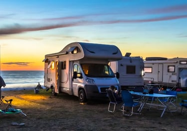 Motorhomes and camper vans parked at a beach campsite during a vibrant sunset over the ocean.