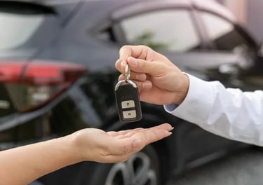 A person handing over electronic car keys to a new owner in front of a black vehicle.