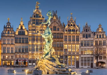 Illuminated Brabo Fountain in front of historic Grote Markt guildhalls in Antwerp, Belgium at dusk.