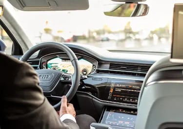 Driver sitting inside a modern Audi luxury sedan featuring a digital cockpit and leather interior.