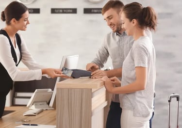 A couple uses a credit card to check in at a hotel reception desk with a smiling concierge.