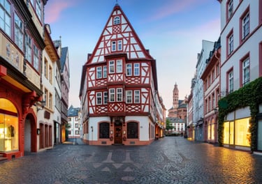 Historic half-timbered building in Mainz old town with cobblestone streets and the cathedral in the distance.