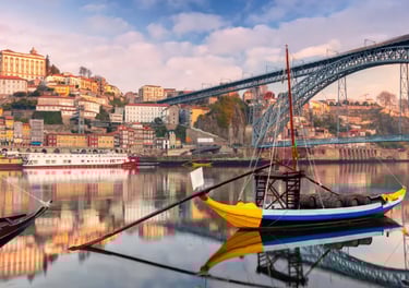 Traditional Rabelo boats on the Douro River with the Dom Luís I Bridge and Porto city skyline in Portugal.
