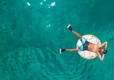Aerial view of a man relaxing on a donut floatie in clear turquoise tropical ocean water.