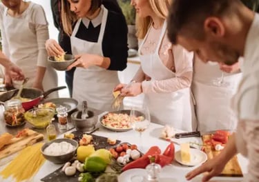 A diverse group of people wearing white aprons during a hands-on Italian cooking class.