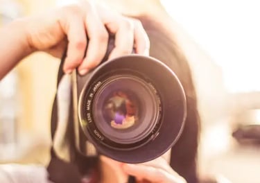 A photographer holding a professional DSLR camera lens with sunlight flare during an outdoor photoshoot.