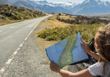A person looks at a map during a scenic road trip with snow-capped mountains in the background.