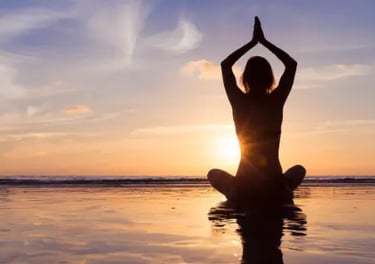 Silhouette of a woman practicing yoga in a seated lotus pose on a beach at sunset.