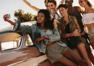 A diverse group of happy friends taking a selfie while leaning against a vintage car on a sunny road trip.