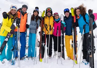 A group of diverse friends smiling on a snowy mountain with their skiing and snowboarding gear.