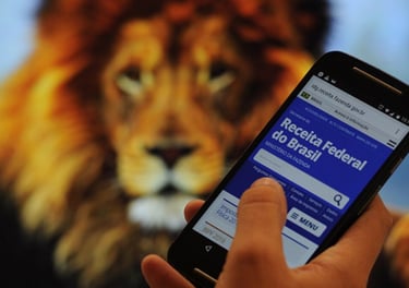 Pessoa segurando celular com site da Receita Federal aberto, ao fundo imagem de leão.