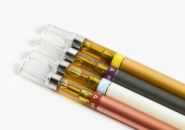 Four cannabis vape cartridges with golden distillate oil attached to colorful slim battery pens.