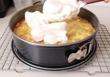 Spreading fluffy white meringue over a freshly baked apple tart in a springform pan on a cooling rack.