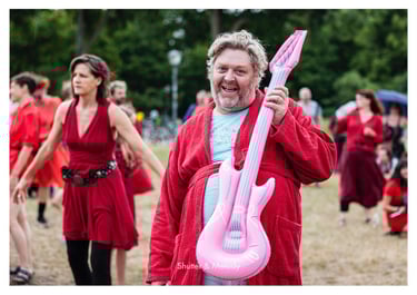 Ein lächelnder Mann im Bademantel mit einer rosa aufblasbaren Gitarre.