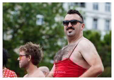 Ein Mann mittleren Alters mit behaarter Brust, rotem Kleid und Sonnenbrille.