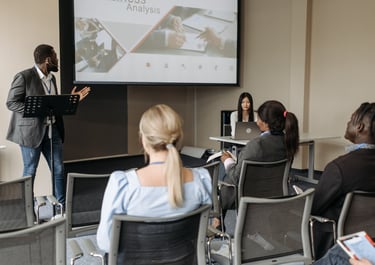 a man in a suit and tie is doing a presentation while others sitting and listening