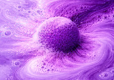 Extra large purple bath bomb fizzing in water with thick foam and cloud-like bubbles.