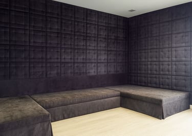Modern corner design with custom upholstered wall panels and matching L-shaped seating in dark fabric by Solo Home Decor.