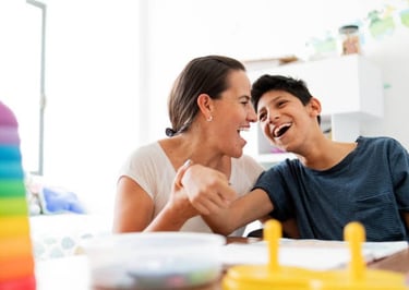 A woman and a boy share a joyful moment, laughing together at a table.