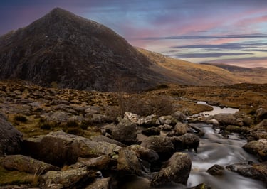 Dramatic sunset clouds over snow-capped mountains and a dark forest landscape.