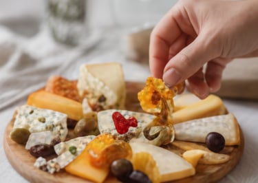 A close-up photo of hands selecting items from a gourmet savory platter with cheeses, grapes, and breads.
