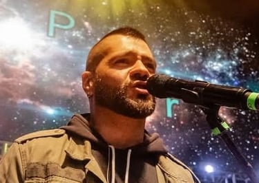 Un cantante masculino con barba interpretando en vivo en el escenario con un micrófono 
