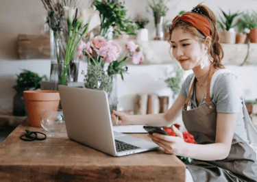 A small businesswoman ownwer sitting on her desk with her laptop and a mobile phone on her hand