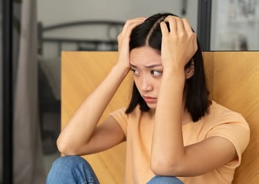 Une femme assise au sol, les mains sur la tête, exprimant une émotion de détresse ou d’angoisse.