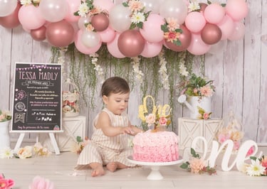 a baby girl in a pink dress and a pink cake
