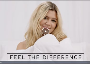 Blonde woman smiling in white bedding with Feel the Difference text overlay.