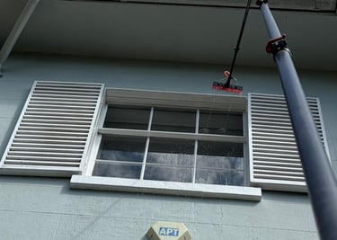 a pole with a brush head attached to it spraying a window