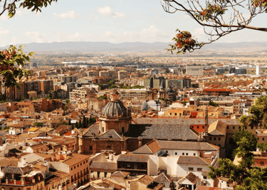Panoramic cityscape view of Granada, Spain, featuring red-tiled roofs and the historic church of San Jeronimo.