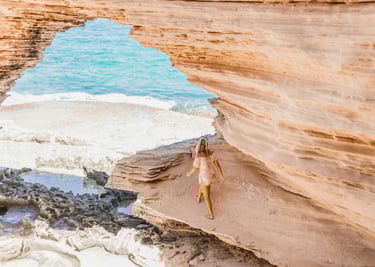 Woman walking along coastal cliff edge overlooking sandy beach and Ocean