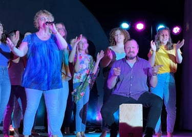 eine Gruppe auf der Bühne, singend, klatschend, ein Mann mit der Cajon dabei