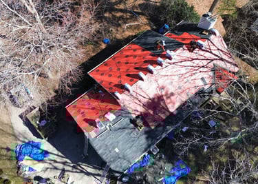 Aerial view of contractors installing new roof shingles over red underlayment on a residential home.