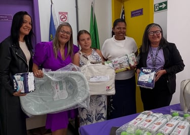 Five women holding newborn baby kits with diapers and a bathtub for maternity donation.