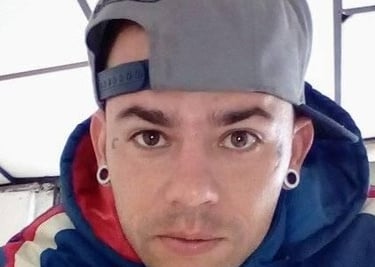 Retrato de un hombre con una gorra gris tipo snapback, sudadera azul con capucha y dilataciones 