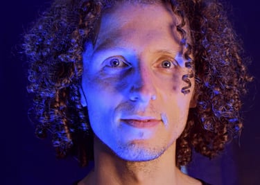 Retrato de un hombre con cabello castaño rizado, iluminado con una dramática luz de estudio azul y c