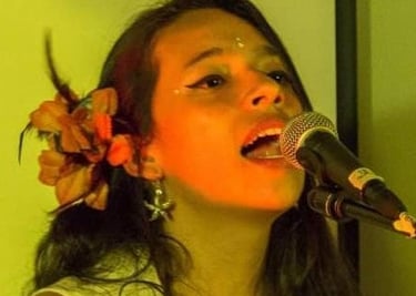 Cantante femenina con una flor en el cabello, interpretando en vivo frente a un micrófono 
