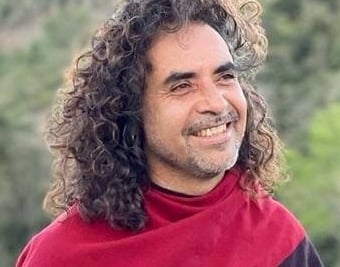 Hombre sonriente con cabello largo, rizado y castaño, usando una camiseta de rayas rojas y negras al