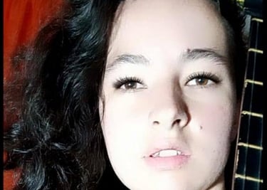 Una joven con cabello largo, oscuro y ondulado, posando de cerca junto al diapasón de su guitarra 