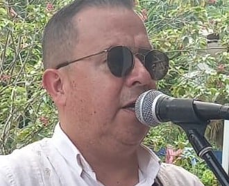 Vocalista masculino con una guayabera blanca y gafas de sol, cantando en un micrófono profesional al