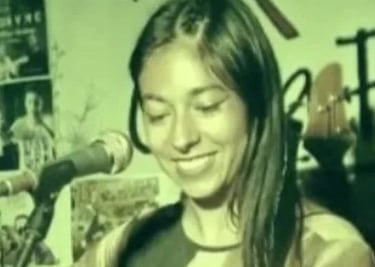 Fotografía vintage con tono verdoso de una cantante de folk sonriente, interpretando con micrófono