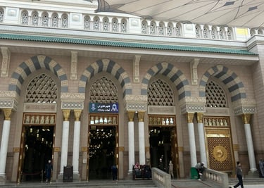 Ornate arched entrances of the Prophet's Mosque in Medina with white umbrellas and marble flooring.